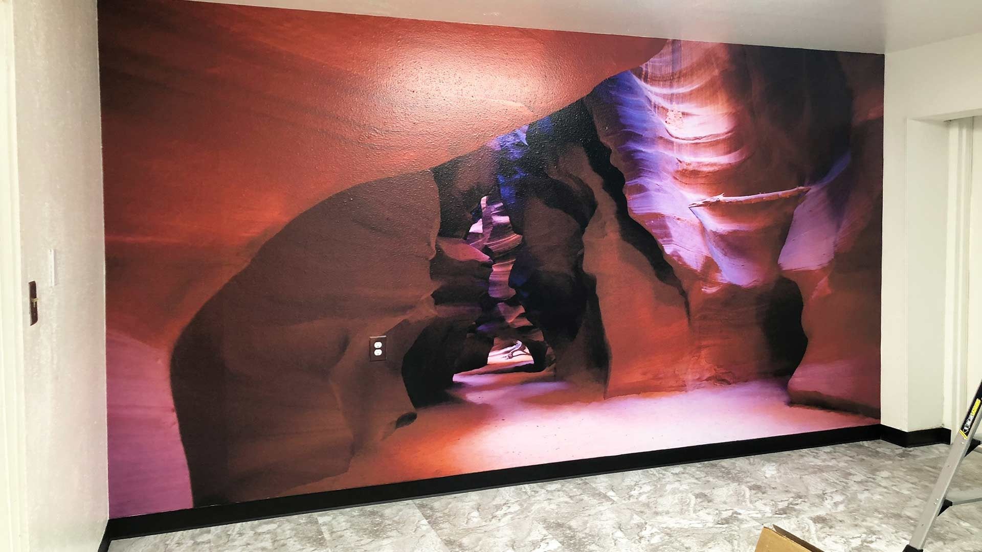 A large mural of a slot canyon with smooth, wavy sandstone walls in hues of orange, red, and purple covers a room wall.