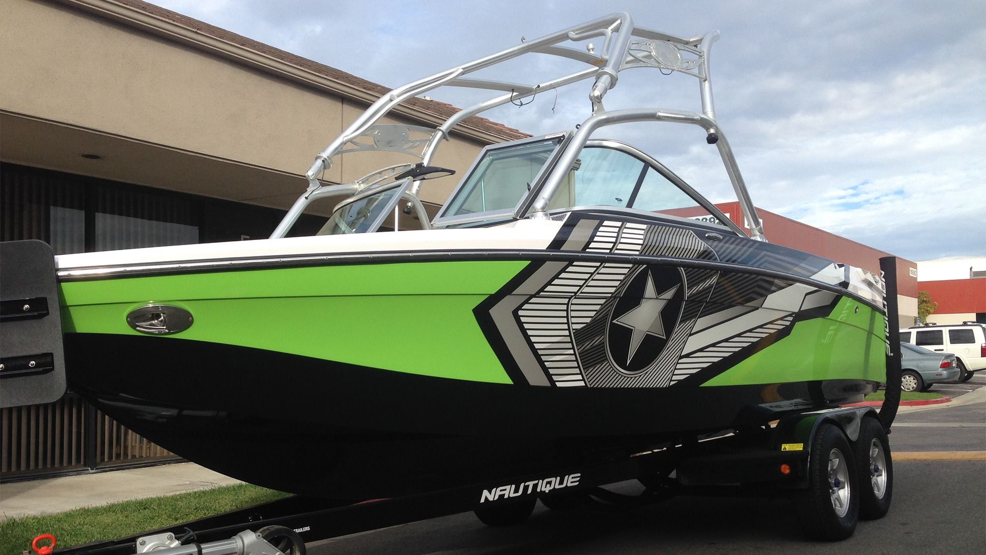 A neon green and black motorboat with a custom star graphic on a trailer, parked outside a building.