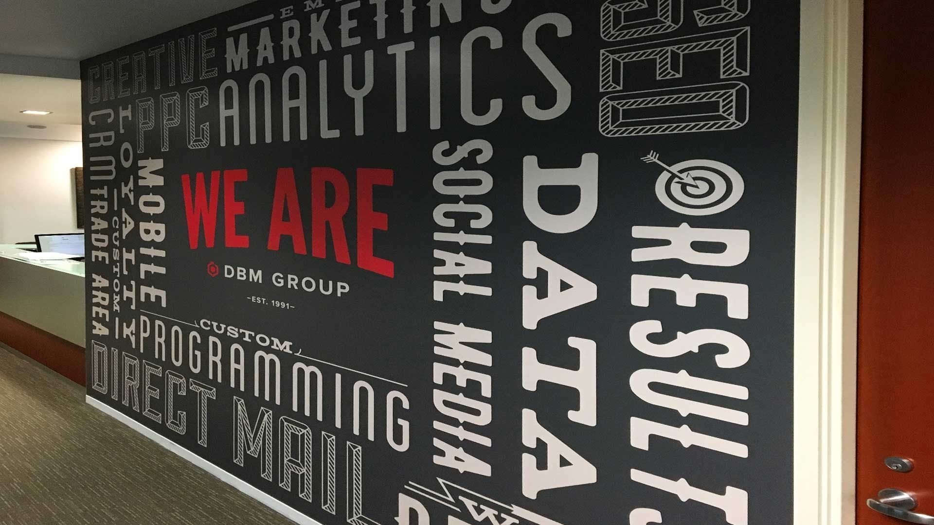 A dark wall mural in an office featuring white word-art text, with the red text 
