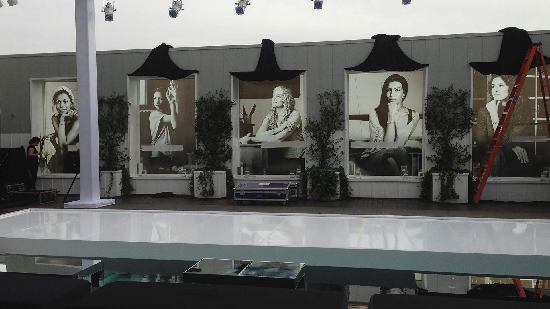 A white table sits before a wall with four large, framed black-and-white portraits and potted plants on a rooftop terrace.