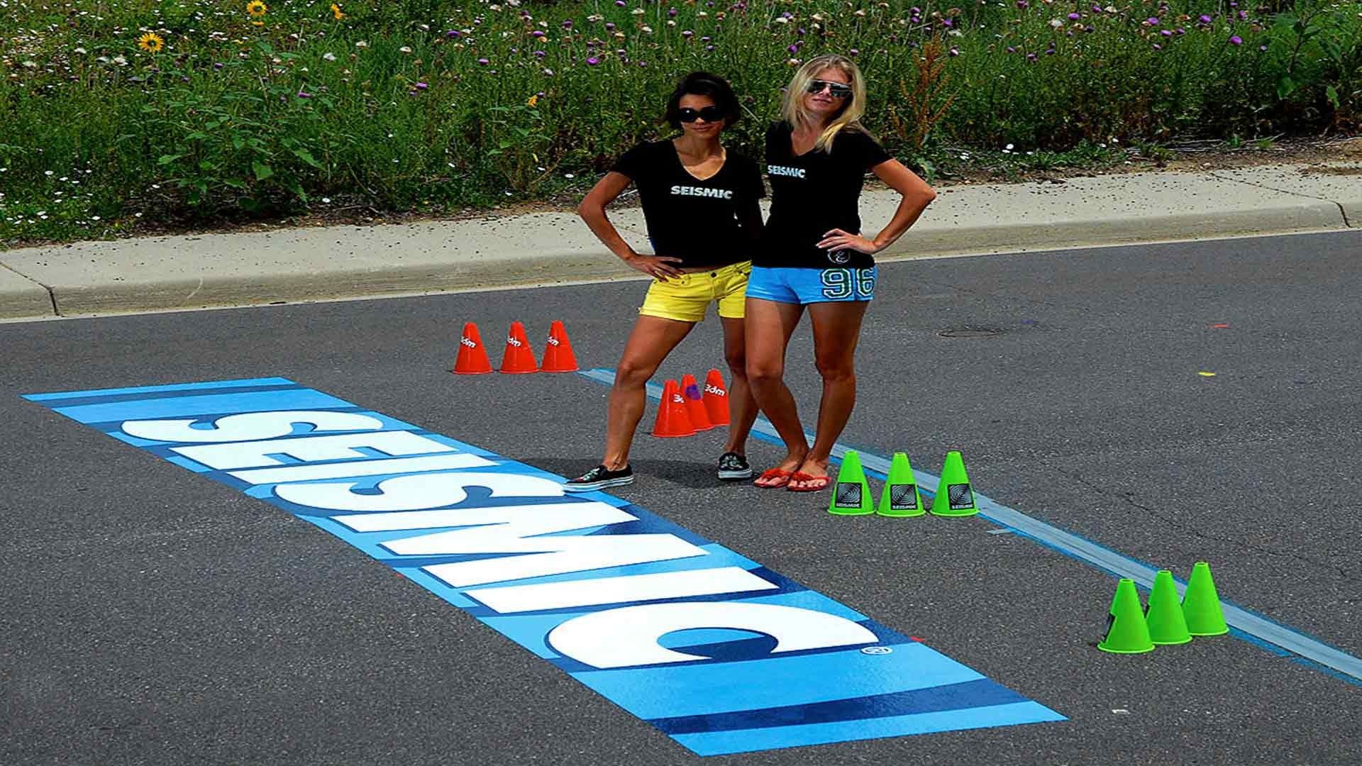 Two individuals stand on pavement near the word 