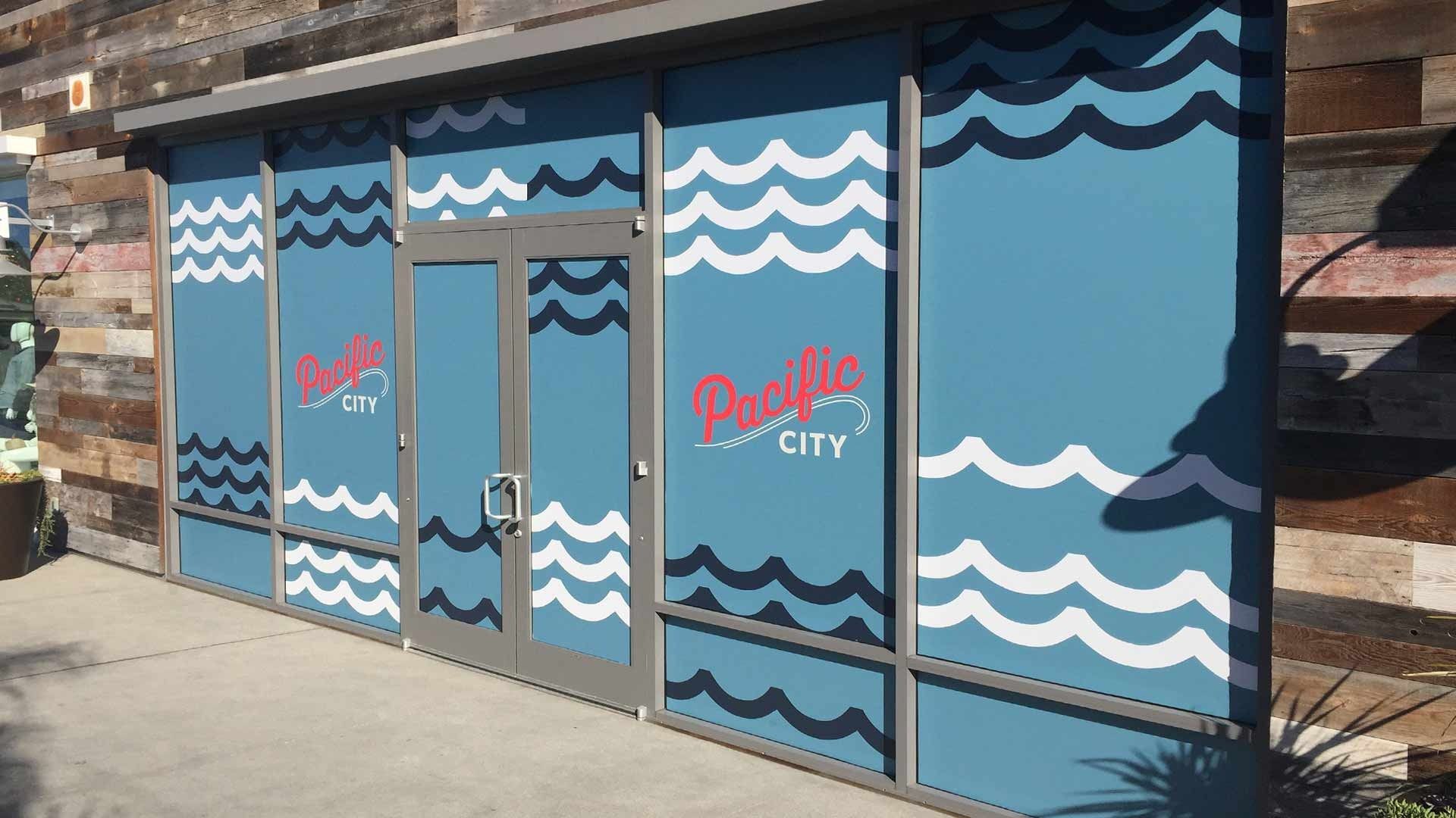 Exterior glass storefront at Pacific City featuring a blue, white-and-dark-blue wave pattern design.