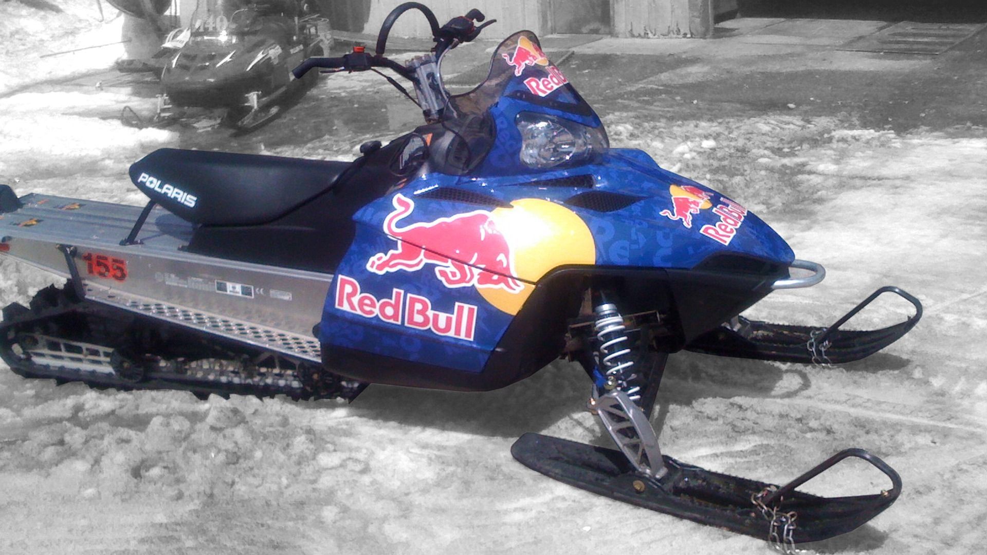 A Red Bull branded snowmobile parked on snow, featuring a blue chassis with a large red and yellow logo.