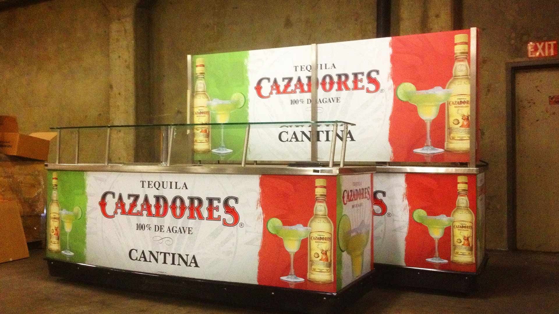 A Cazadores Tequila Cantina bar set-up with red, white, and green branding featuring tequila bottles and lime cocktails.