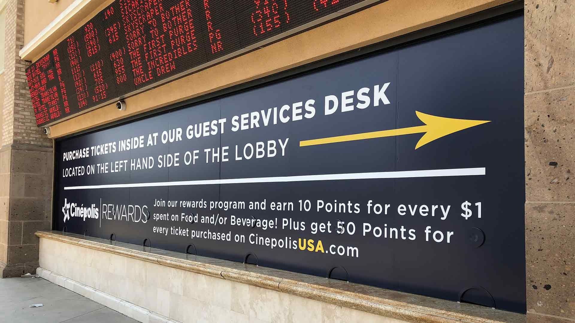 A black sign with yellow text directs guests to the service desk on the left of the lobby at a Cinépolis movie theater.