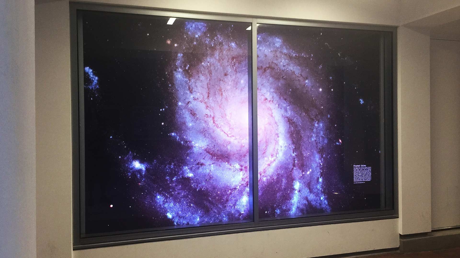 A large digital display set into a wall shows a vibrant, swirling purple and blue spiral galaxy against deep black space.