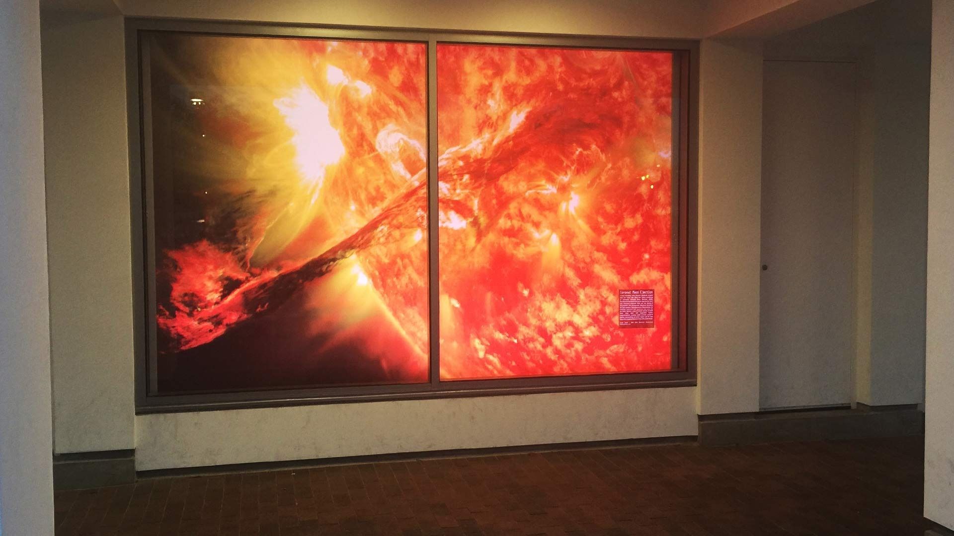 A large, bright, illuminated wall display showing a vibrant, fiery image of the sun in an indoor hallway.