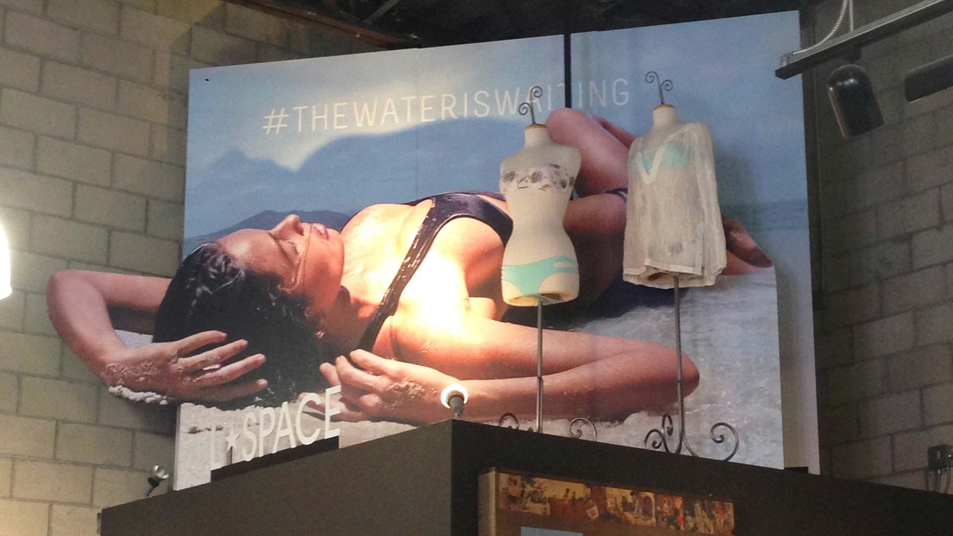 A large store display features a photographic banner of a person lounging, with two torso mannequins showcasing swimwear.