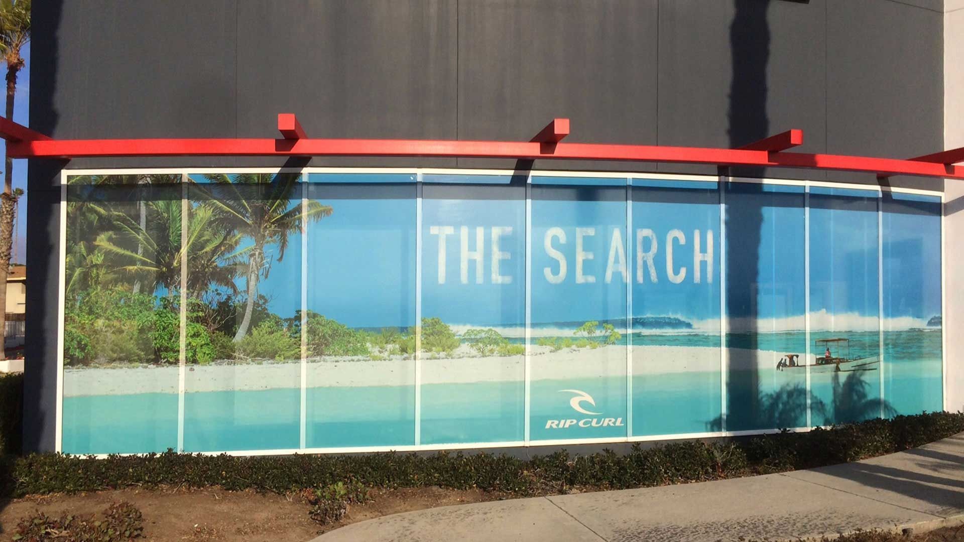 A large window decal on a building exterior displays a tropical beach scene with the text 