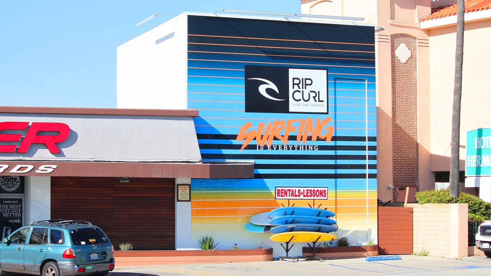 Rip Curl surf shop exterior with a blue and orange mural and surfboards on display in a parking lot.