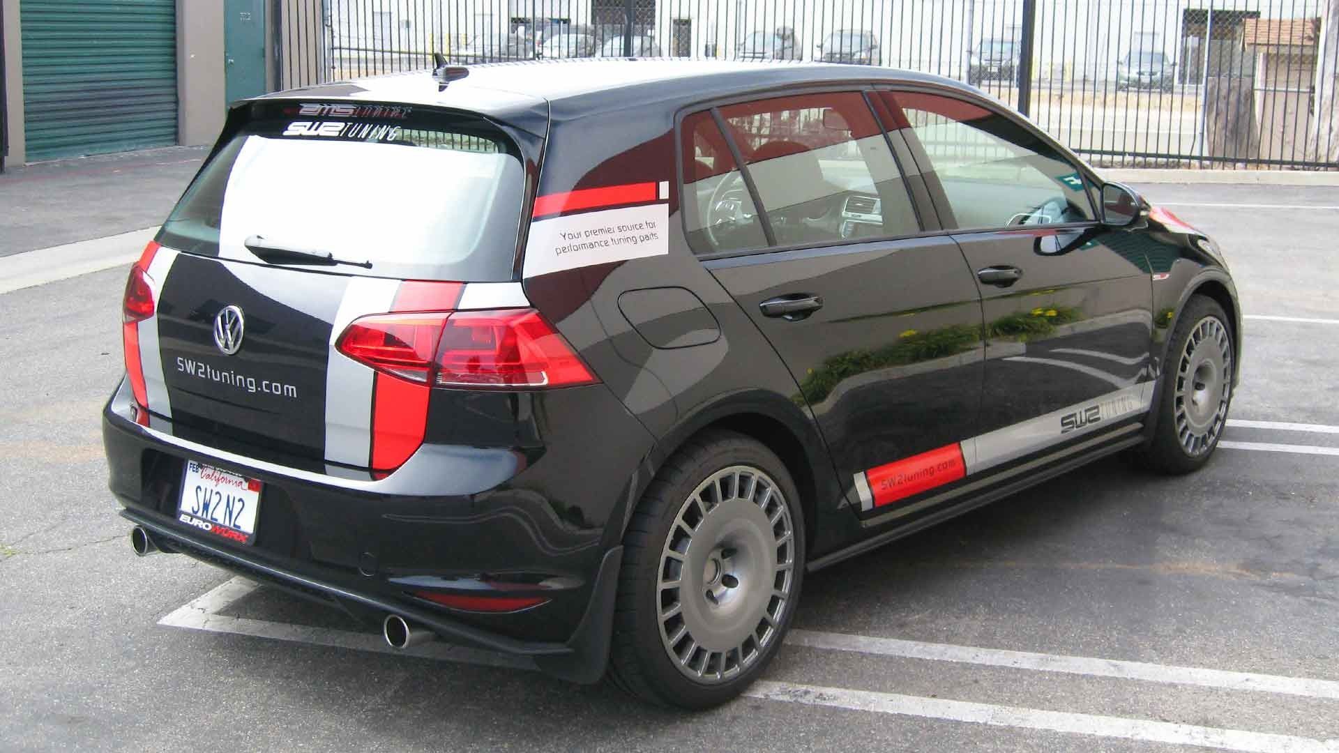 A black Volkswagen Golf hatchback parked in a lot, featuring custom silver and red racing stripes and multi-spoke wheels.