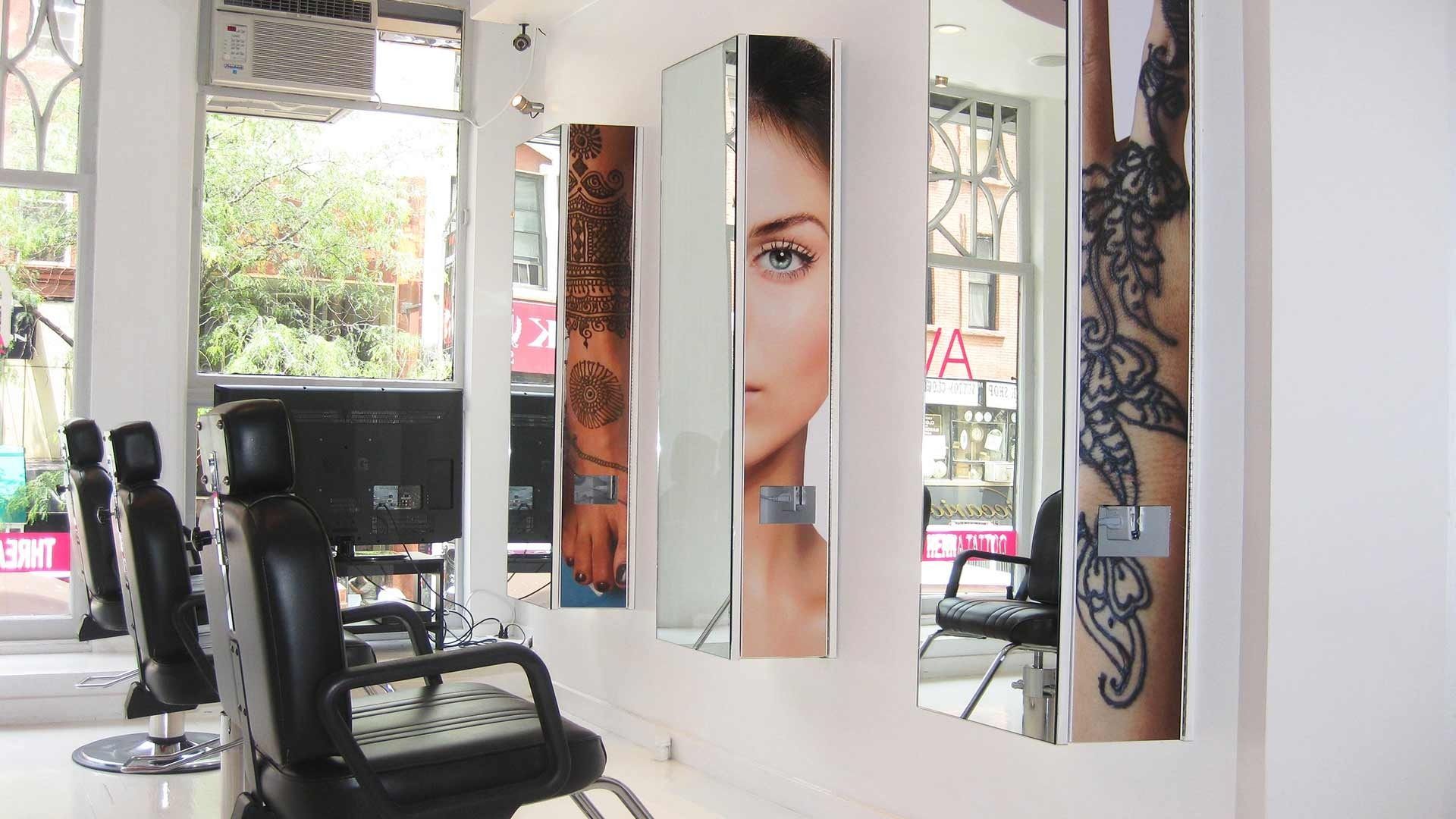 A salon interior featuring two black barber chairs facing large, wall-mounted mirrors decorated with ornate black designs.