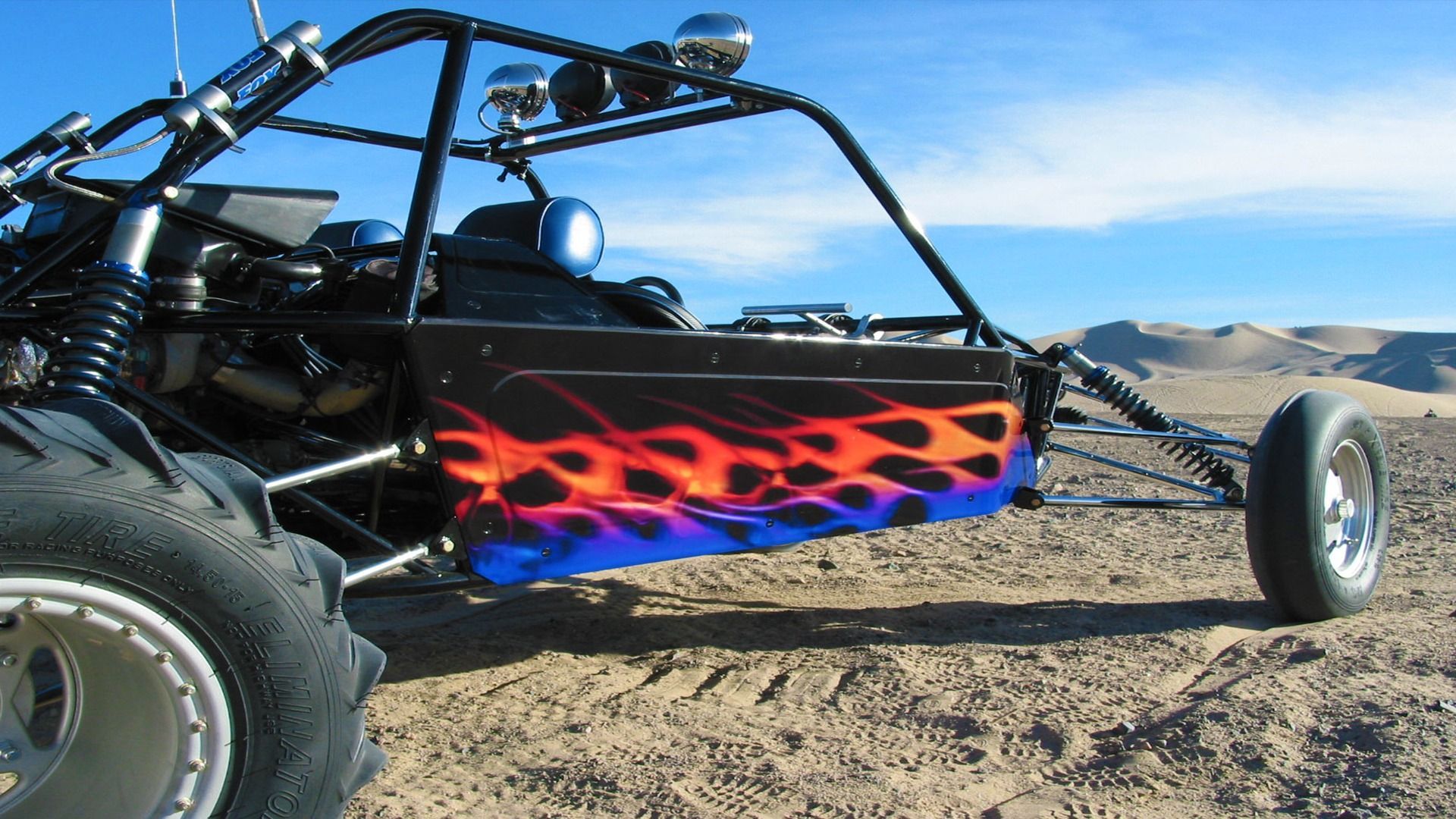 A black off-road sand buggy with flame-patterned side panels parked on a desert dune.