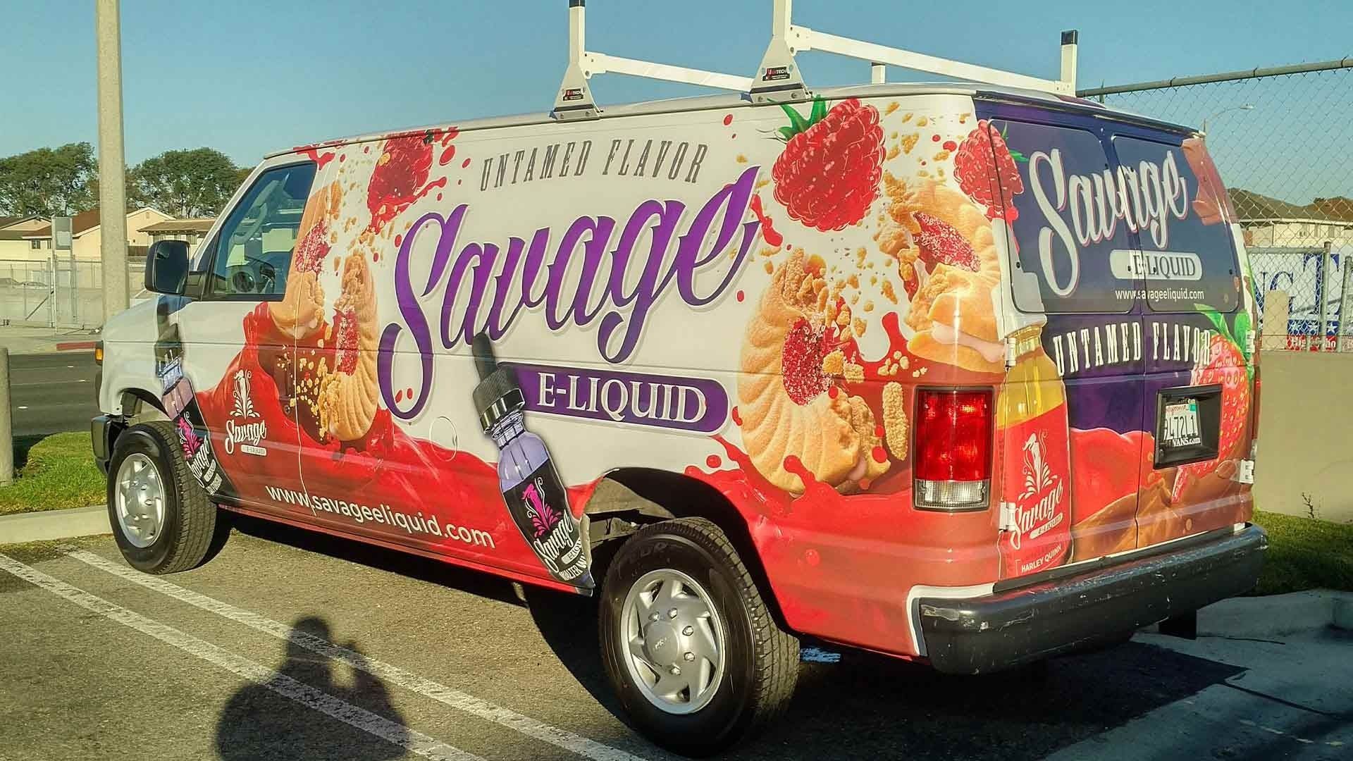 A white van parked outdoors featuring a colorful vehicle wrap for Savage E-Liquid with strawberry and pastry imagery.