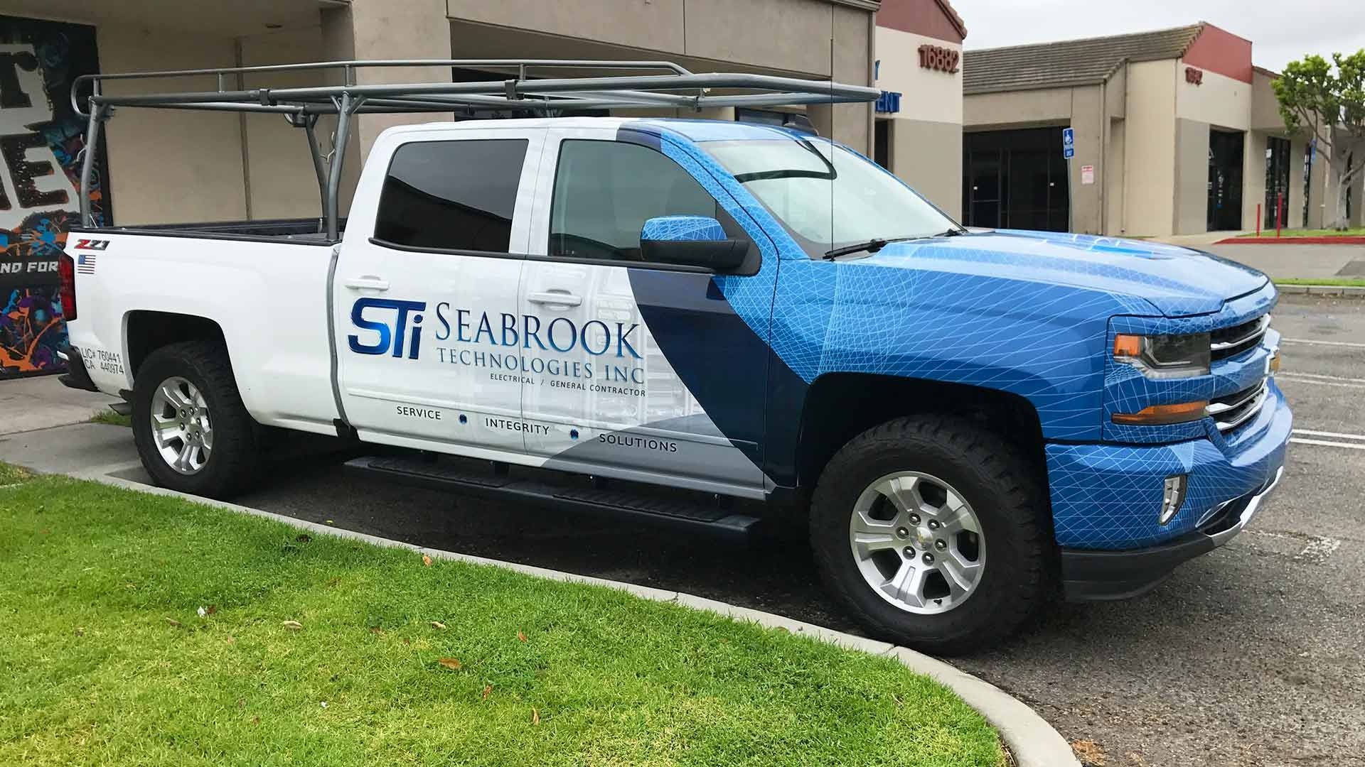 A white and blue Seabrook Trucking & Logistics pickup truck with a roof rack parked on a paved lot.