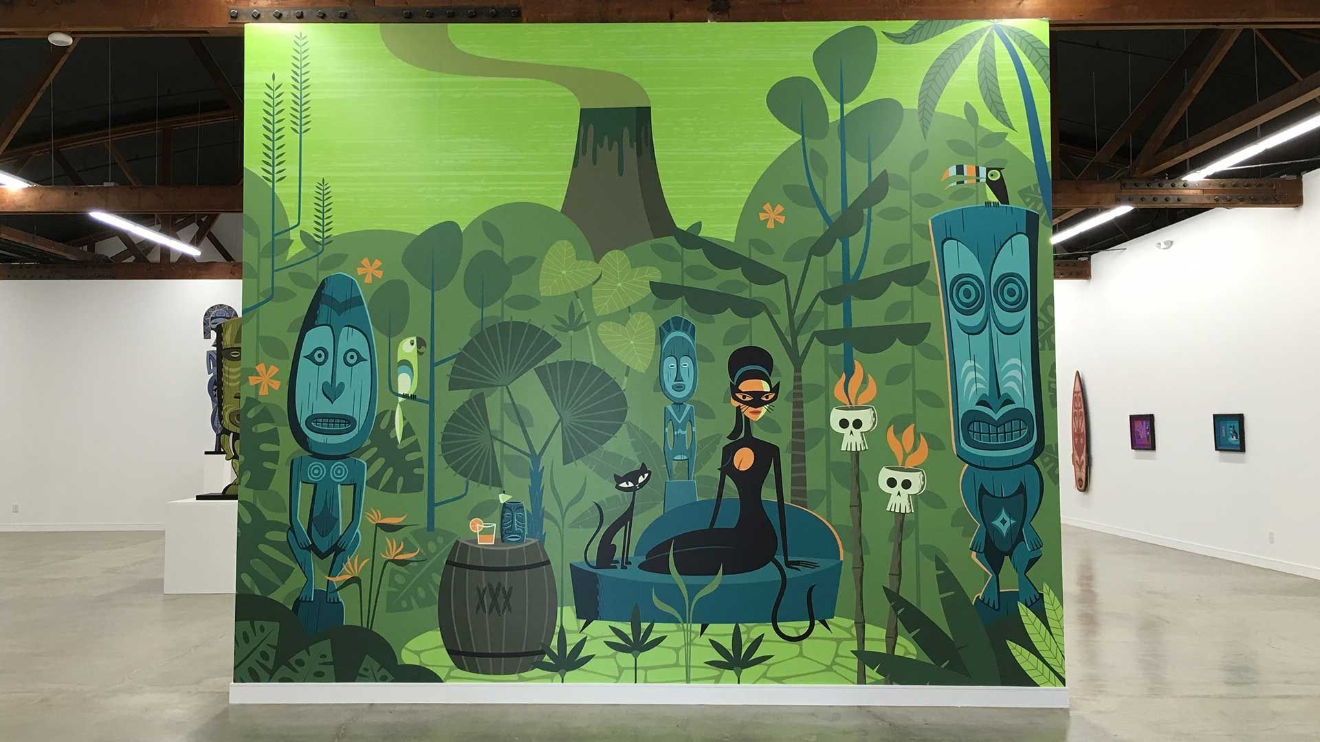 A large, green-hued mural in an art gallery featuring tiki statues, a smoking volcano, and a stylized figure on a bench.