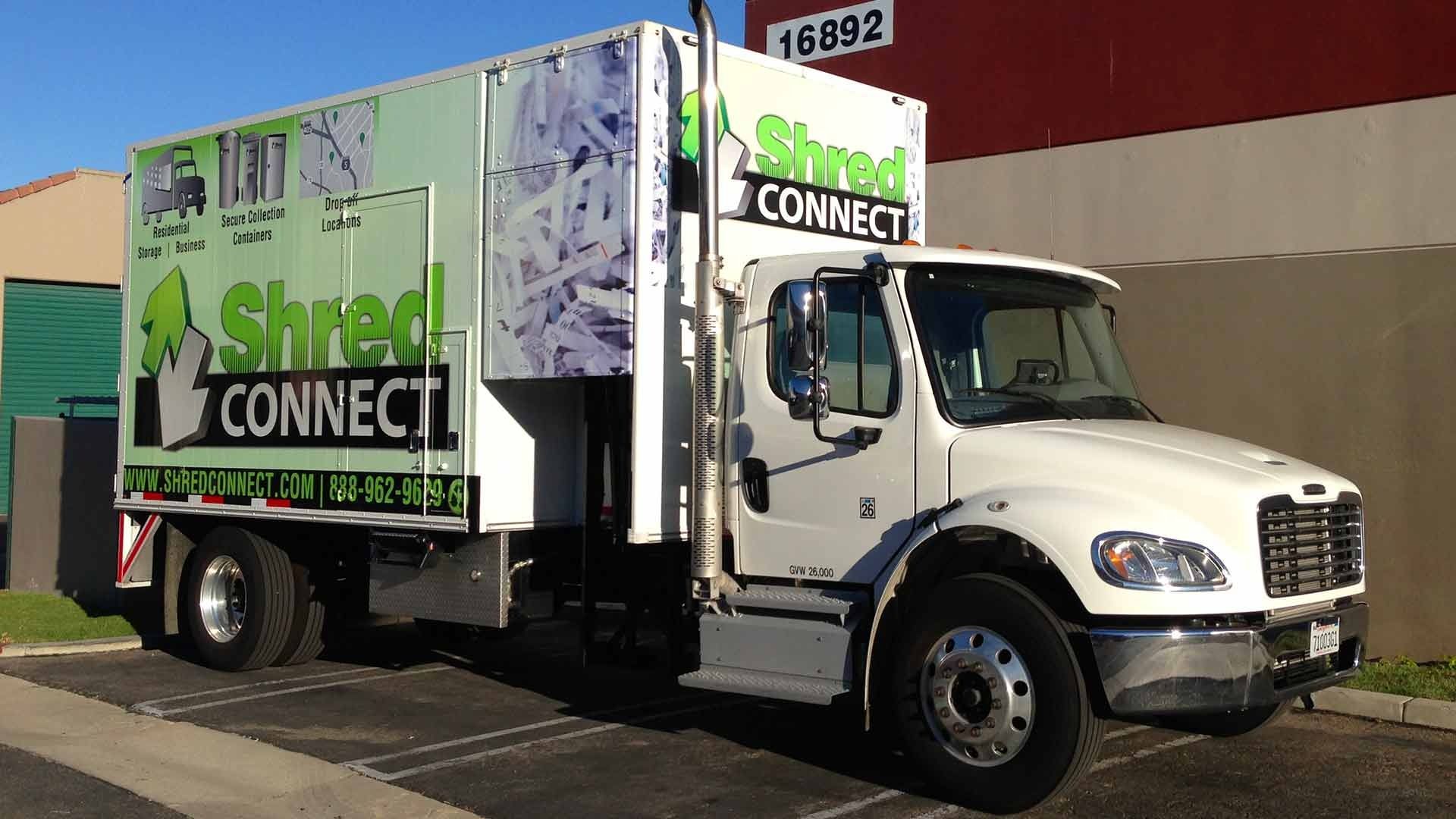 A white Shred Connect box truck parked outside a building with the number 16892 visible on the red exterior wall.
