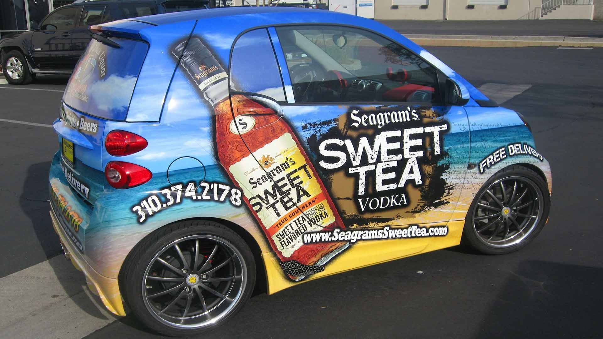 A small car wrapped in a Seagram’s Sweet Tea Vodka advertisement with a beach scene and a large bottle graphic.