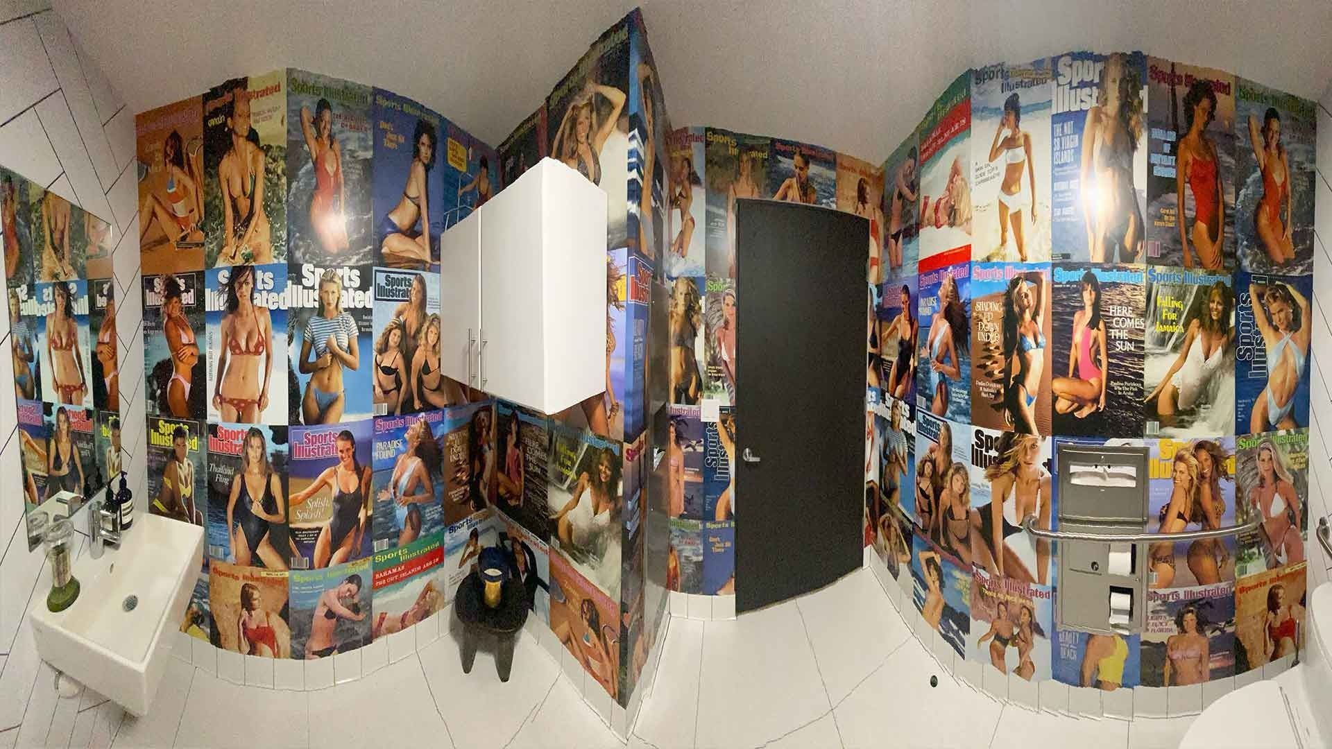 A restroom with walls completely covered in magazine covers featuring models, a white sink, and a dark closed door.