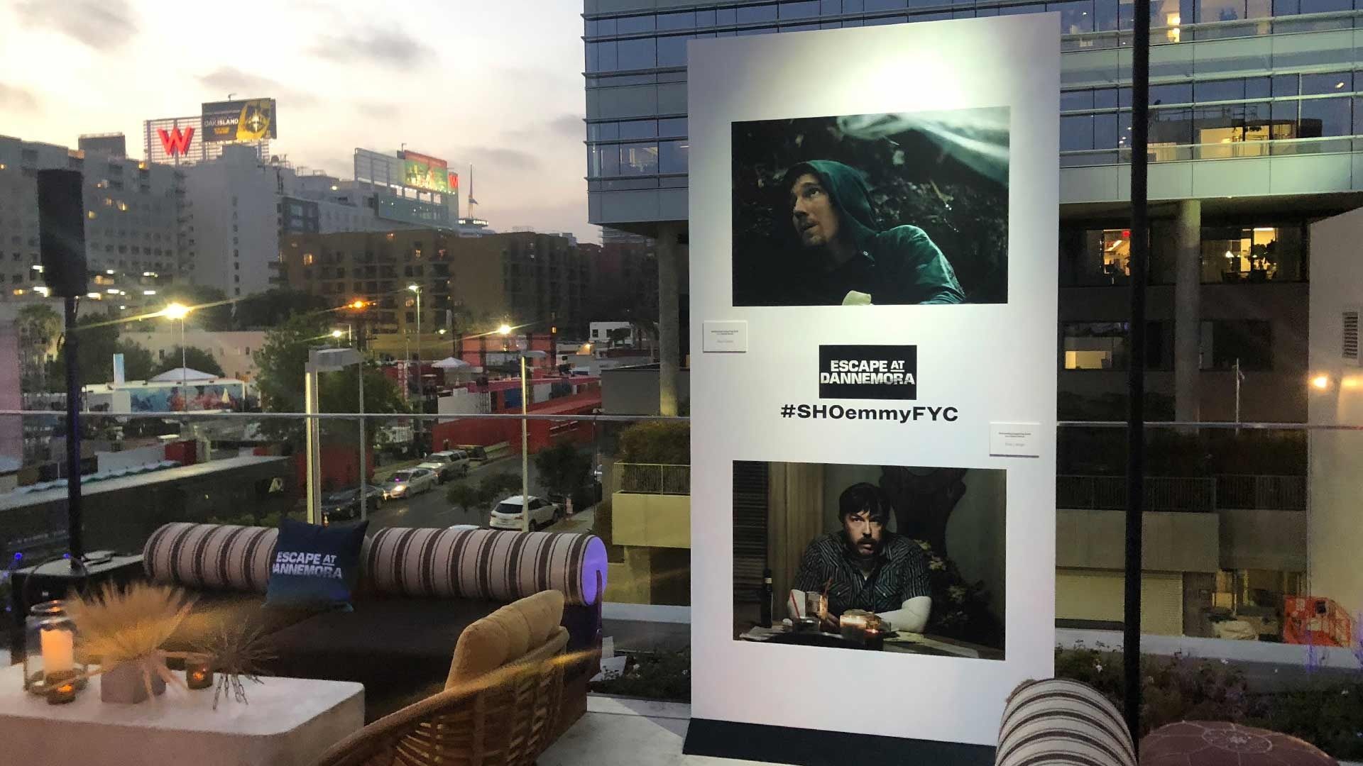 An outdoor lounge at dusk features a display board showing two scenes from a film, with the text 