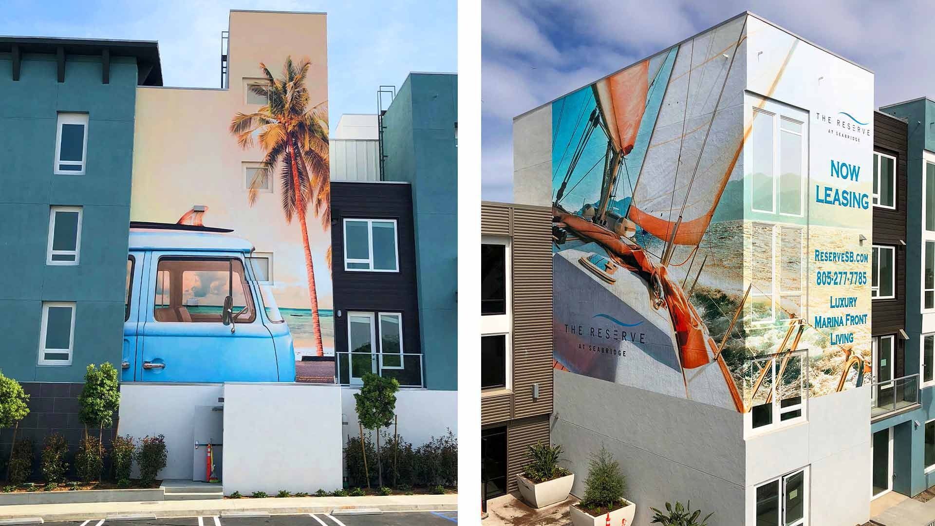 Two apartment buildings featuring large, colorful murals of a blue vintage van and a sailboat on their exterior walls.