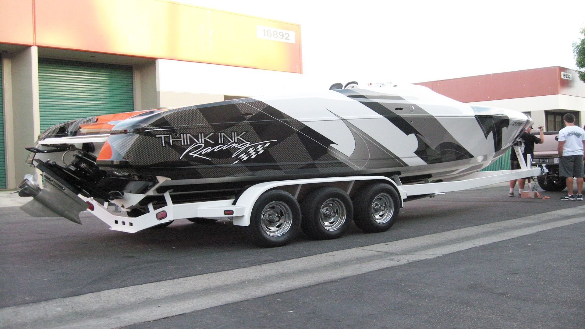 A black, white, and orange performance boat on a triple-axle trailer, parked in front of a building.