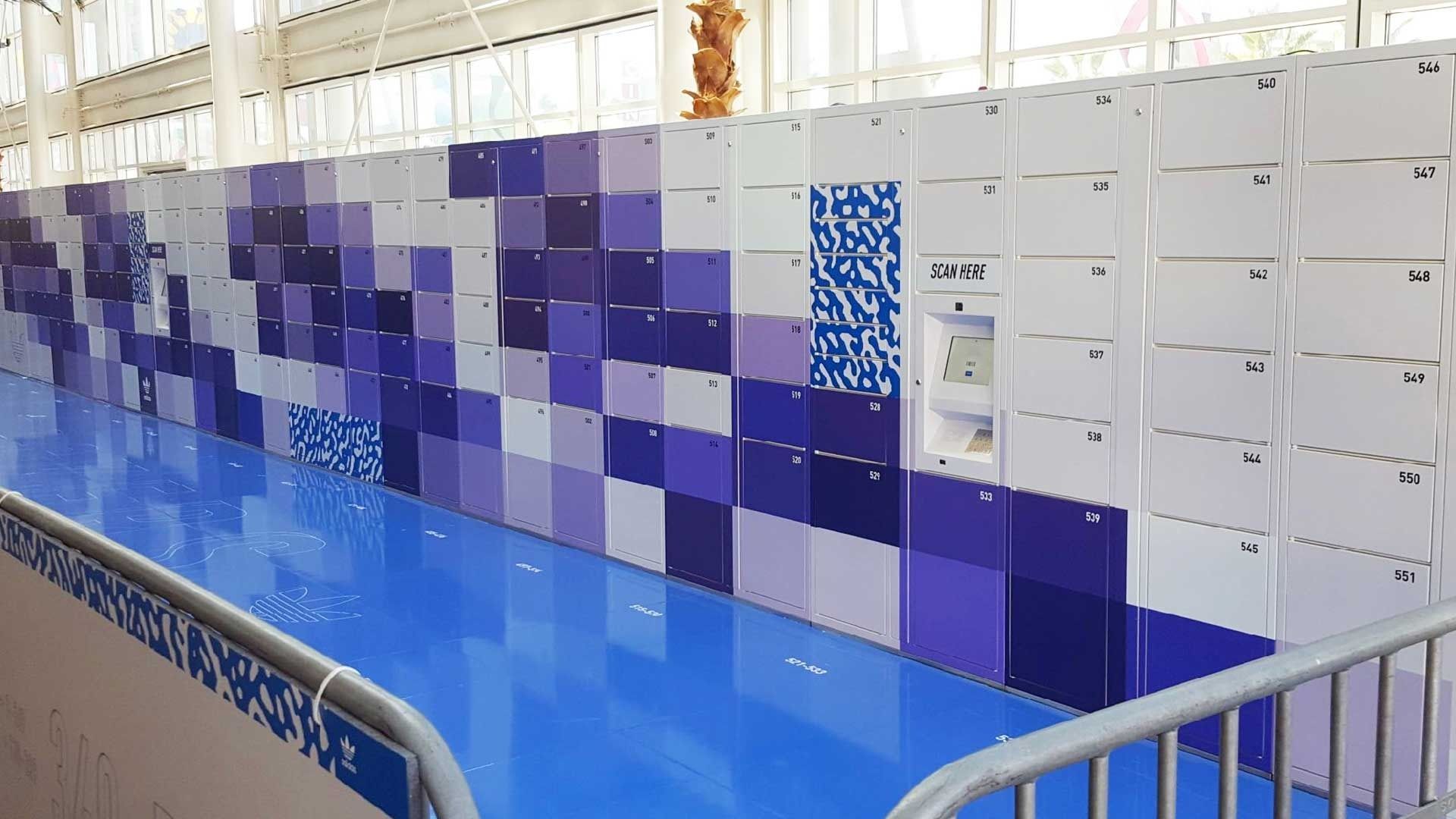 A row of storage lockers in varying shades of blue and white, located along a bright blue floor in a modern facility.
