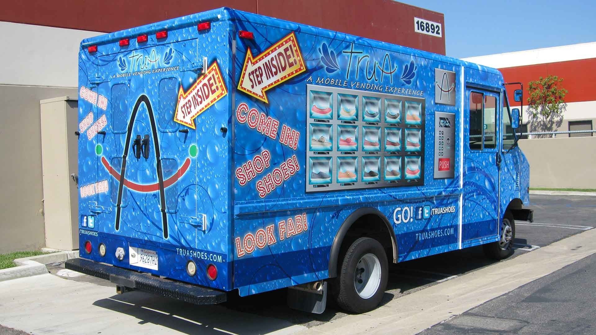 A bright blue truck parked outdoors, featuring a graphic of the St. Louis Gateway Arch and menu photos on the side.