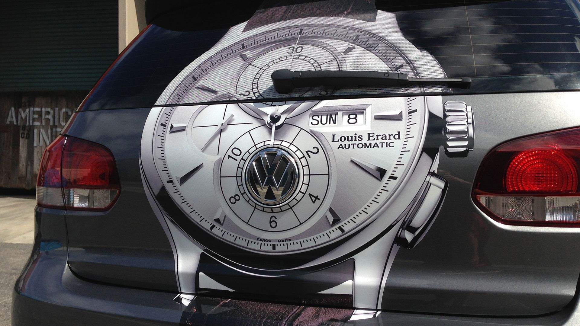A Volkswagen hatchback with a large watch face decal covering the entire rear window.
