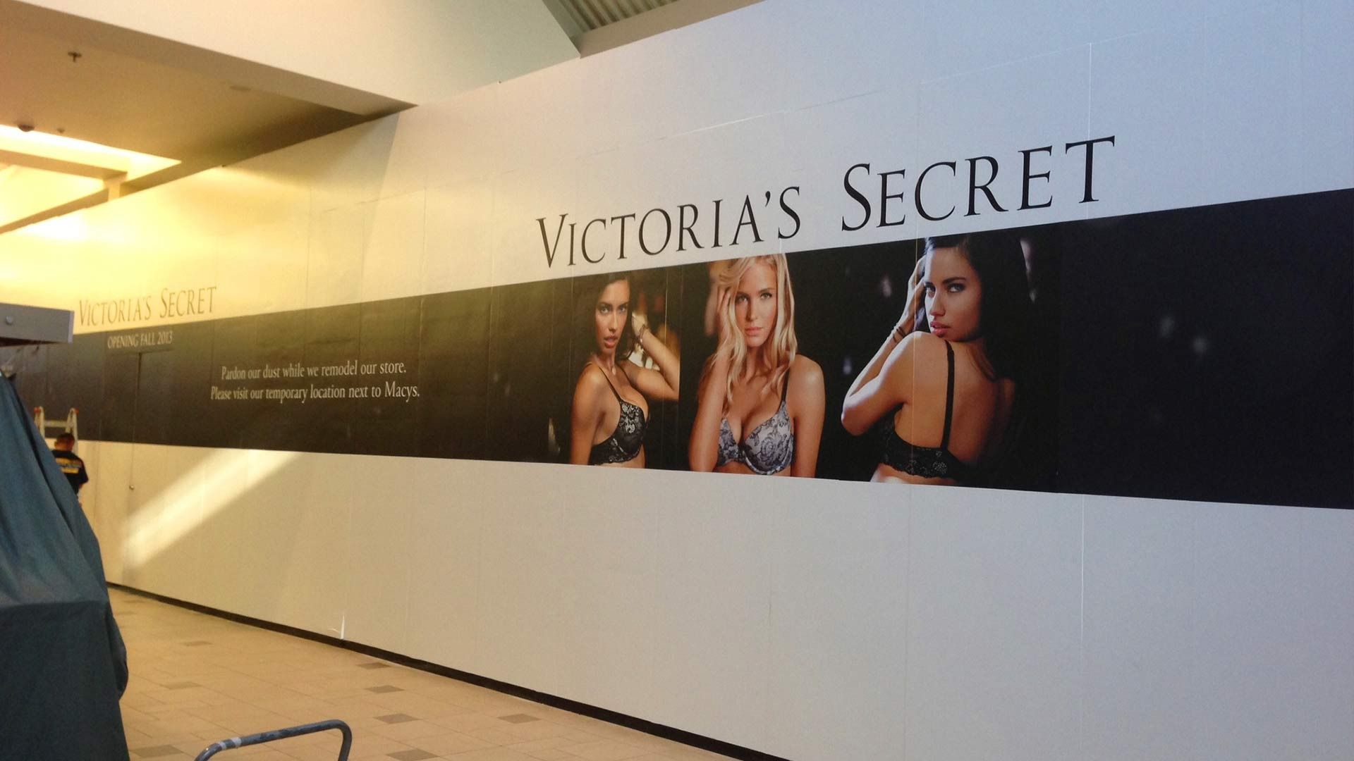 A large Victoria's Secret advertisement banner on a wall in a shopping mall with images of lingerie models.