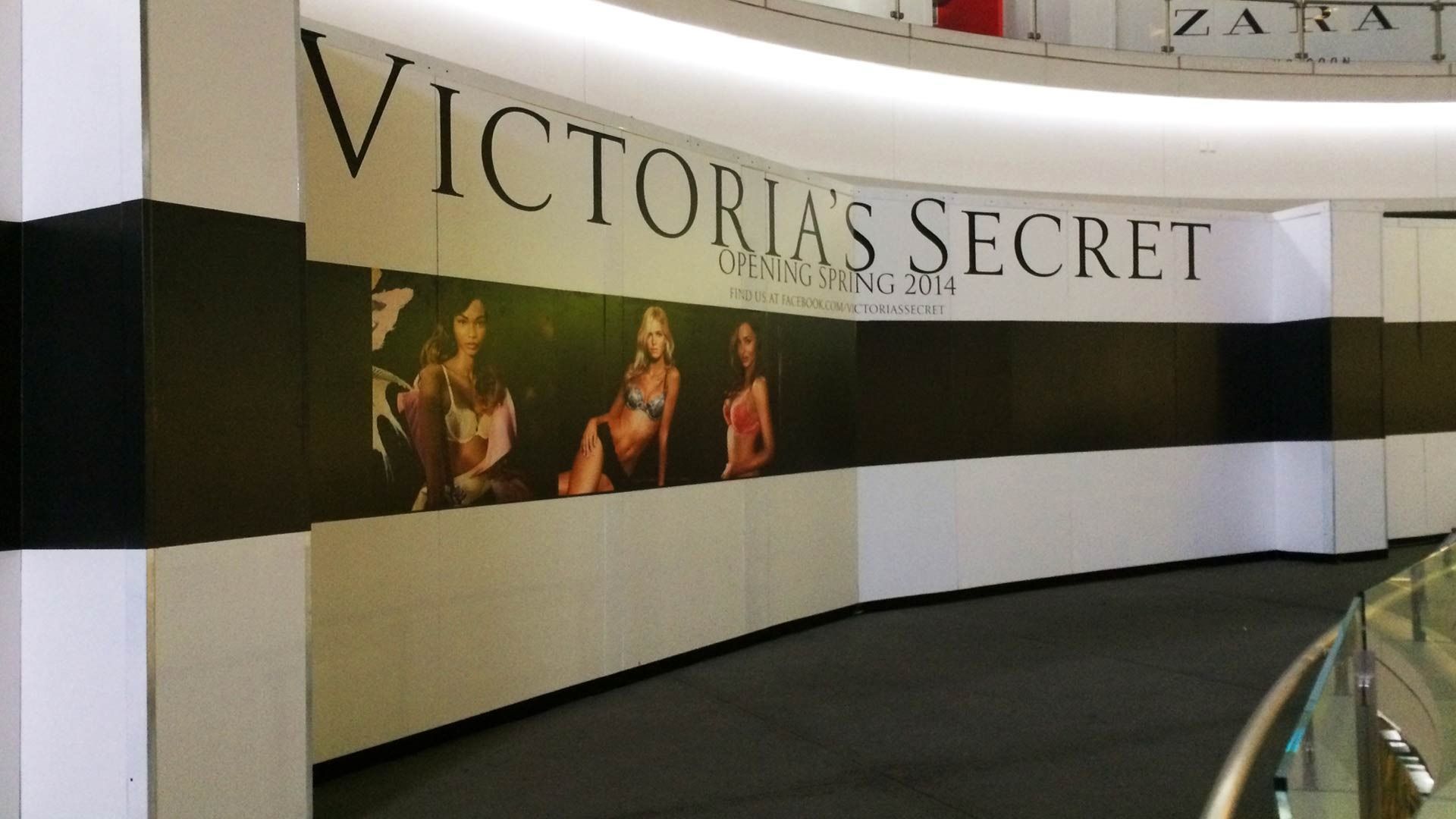 Construction hoarding for a future Victoria’s Secret store, featuring brand signage and models, located in a shopping mall.