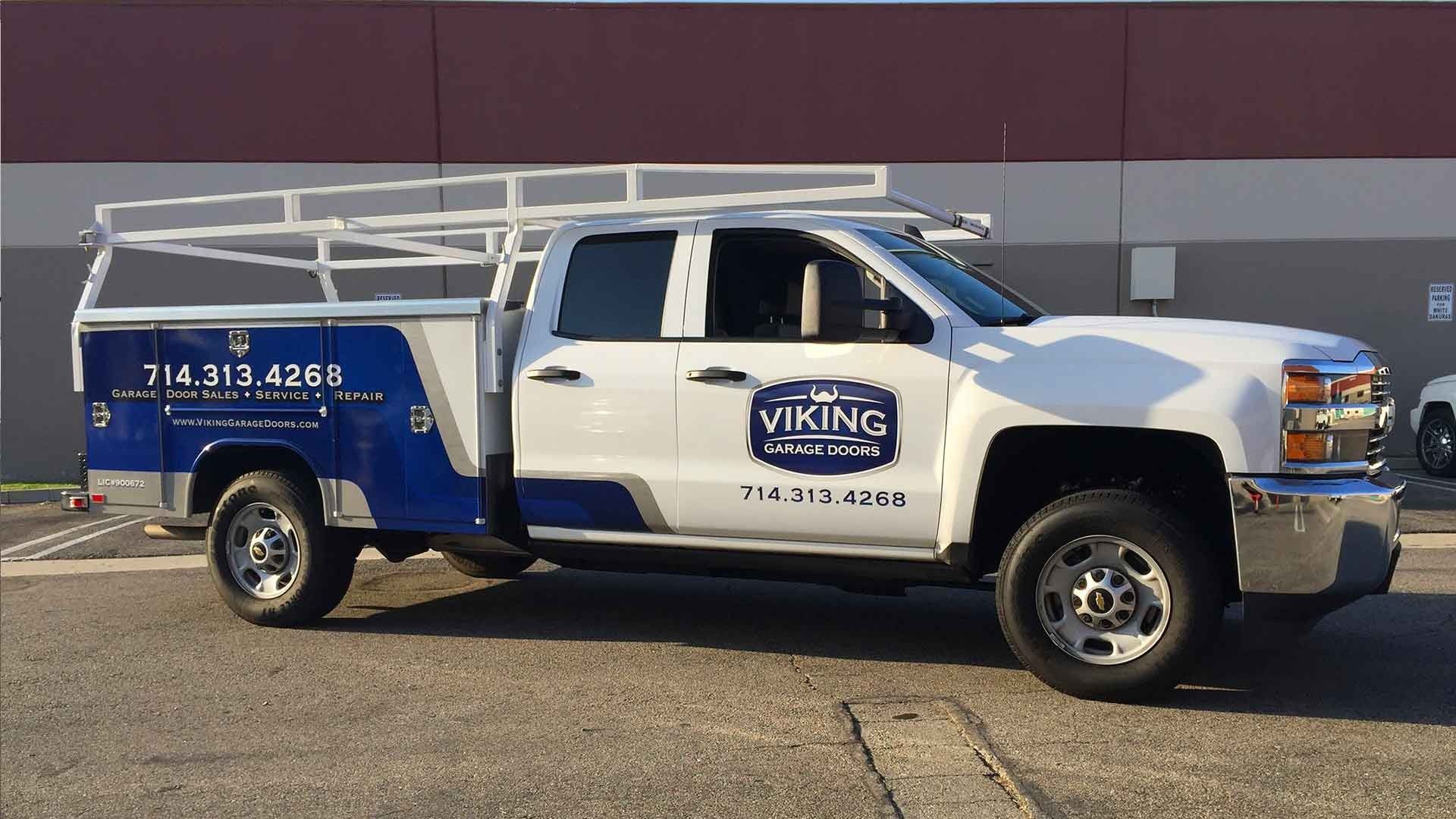 A white and blue service truck with a utility rack and company branding, parked in a parking lot.