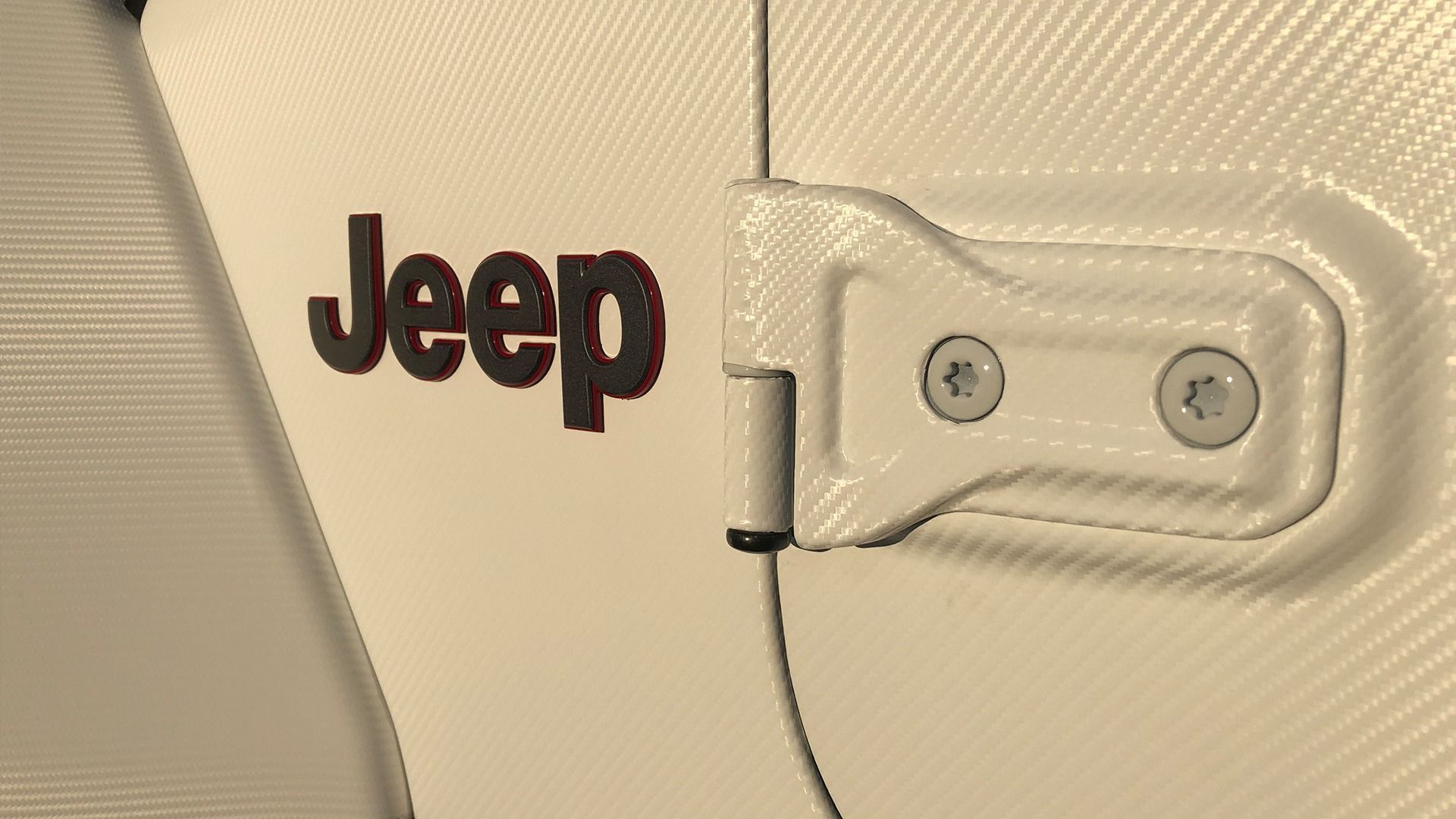 Close-up of a white Jeep vehicle door hinge with a black Jeep logo on the side panel.