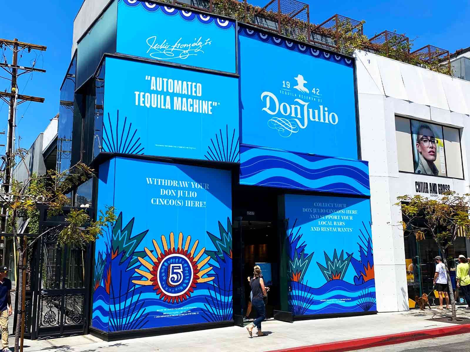 A vibrant blue exterior of a Don Julio pop-up shop on a city street, featuring branding, palm motifs, and an entrance.