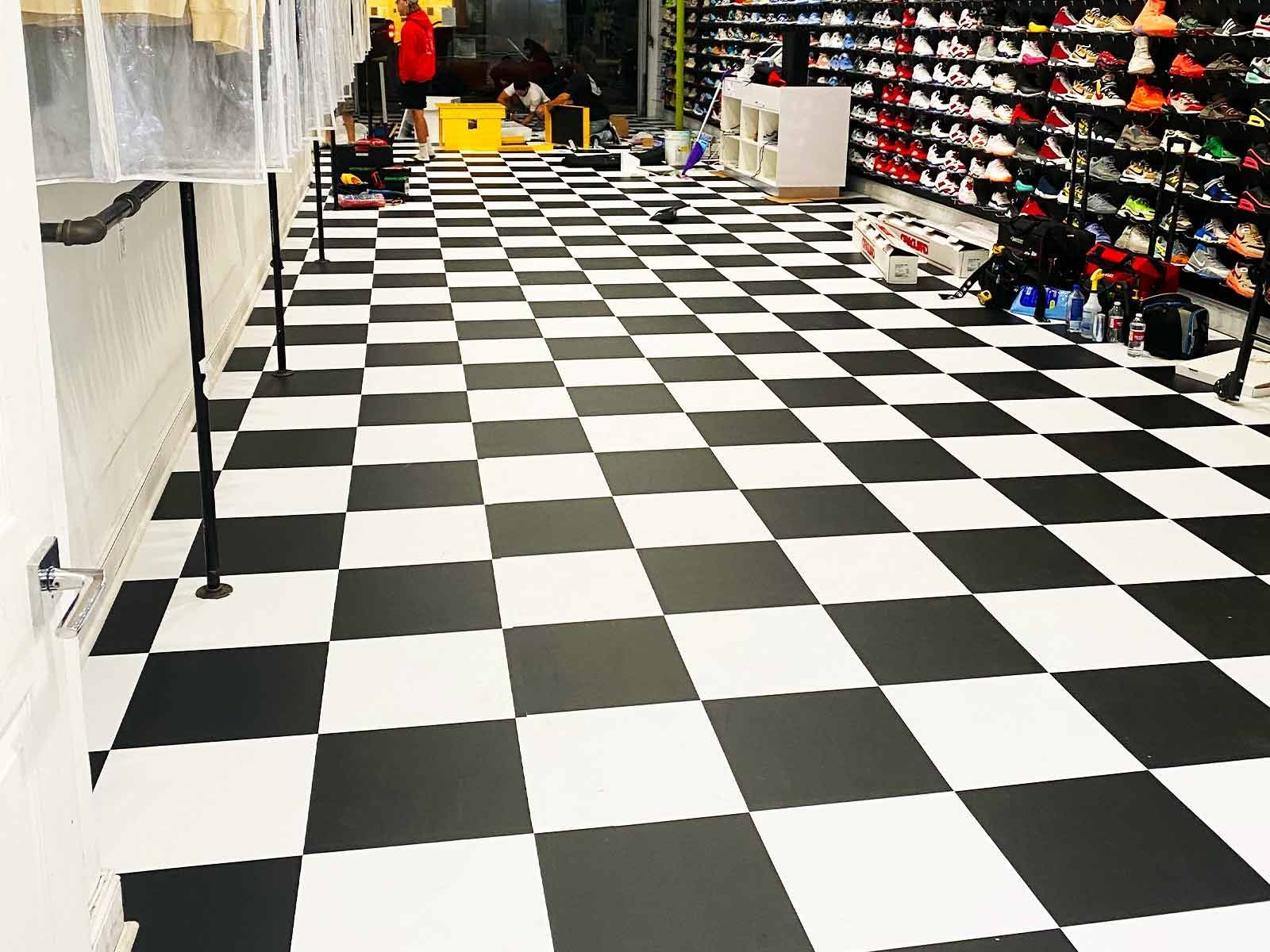 A sneaker store interior with a black and white checkered floor, shelving units filled with shoes, and work equipment.