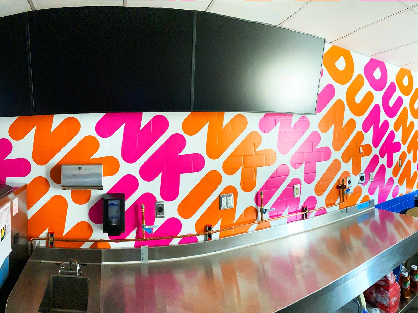 A stainless steel counter in front of a wall featuring a repeating, brightly colored