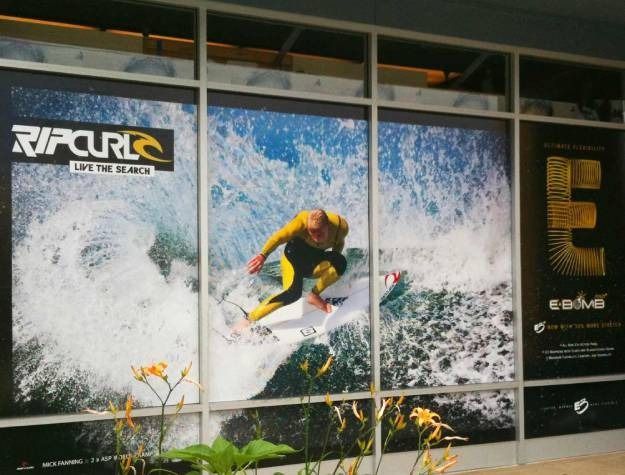 Store window display featuring a Rip Curl surfing advertisement with a surfer riding a large wave.