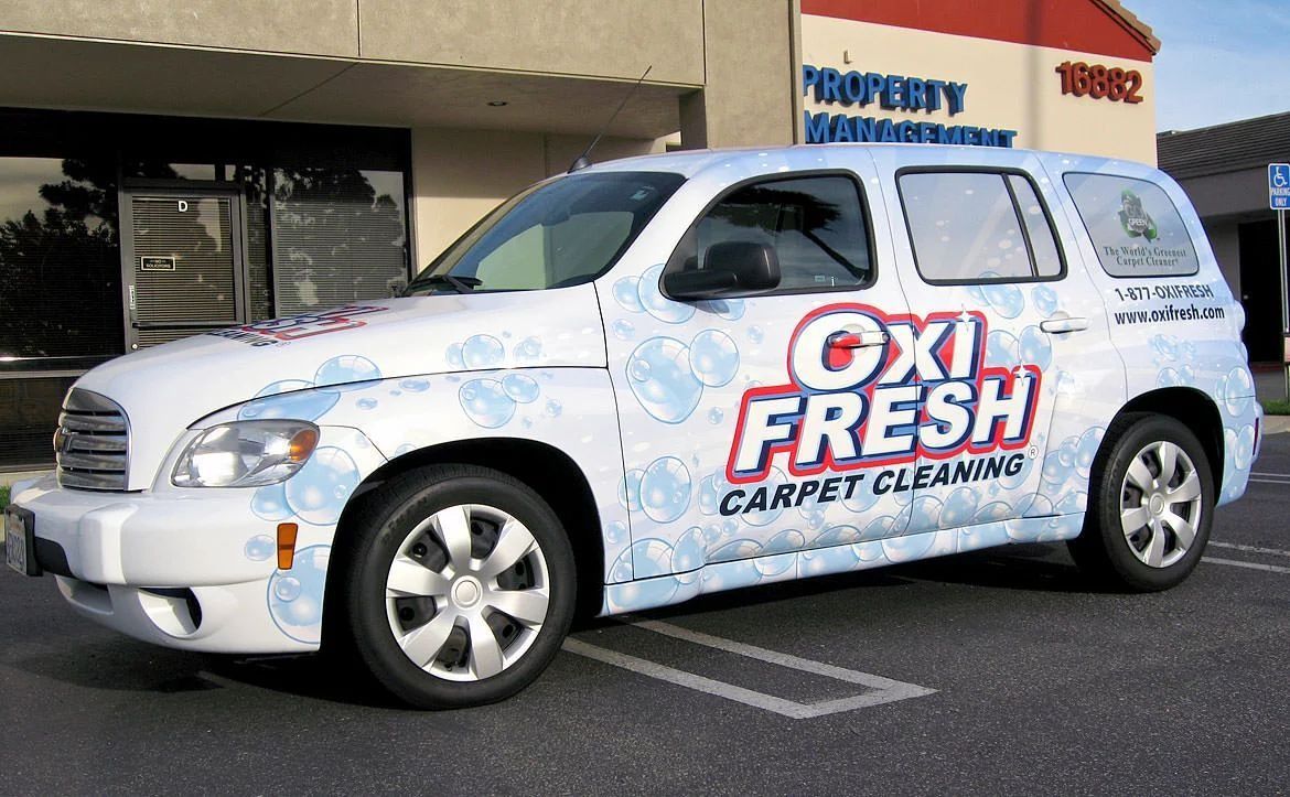 A white Chevrolet HHR parked in a lot, wrapped in blue bubble graphics and Oxi Fresh Carpet Cleaning branding.