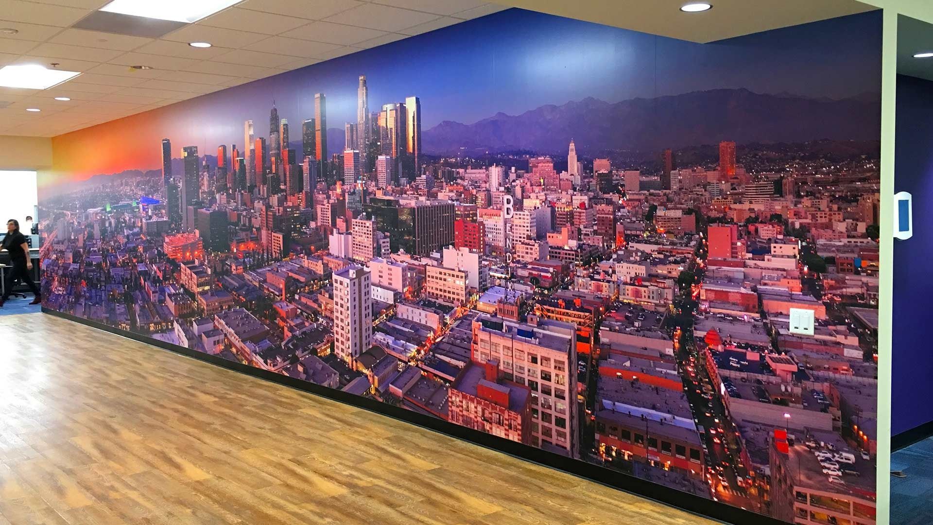A floor-to-ceiling city skyline mural covers a wall in a bright, modern office with wooden floors.