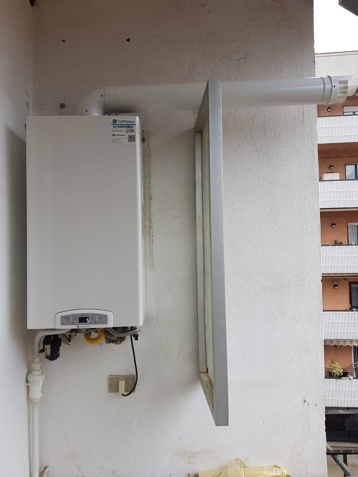 Una caldaia bianca è montata su una parete bianca accanto a una finestra.