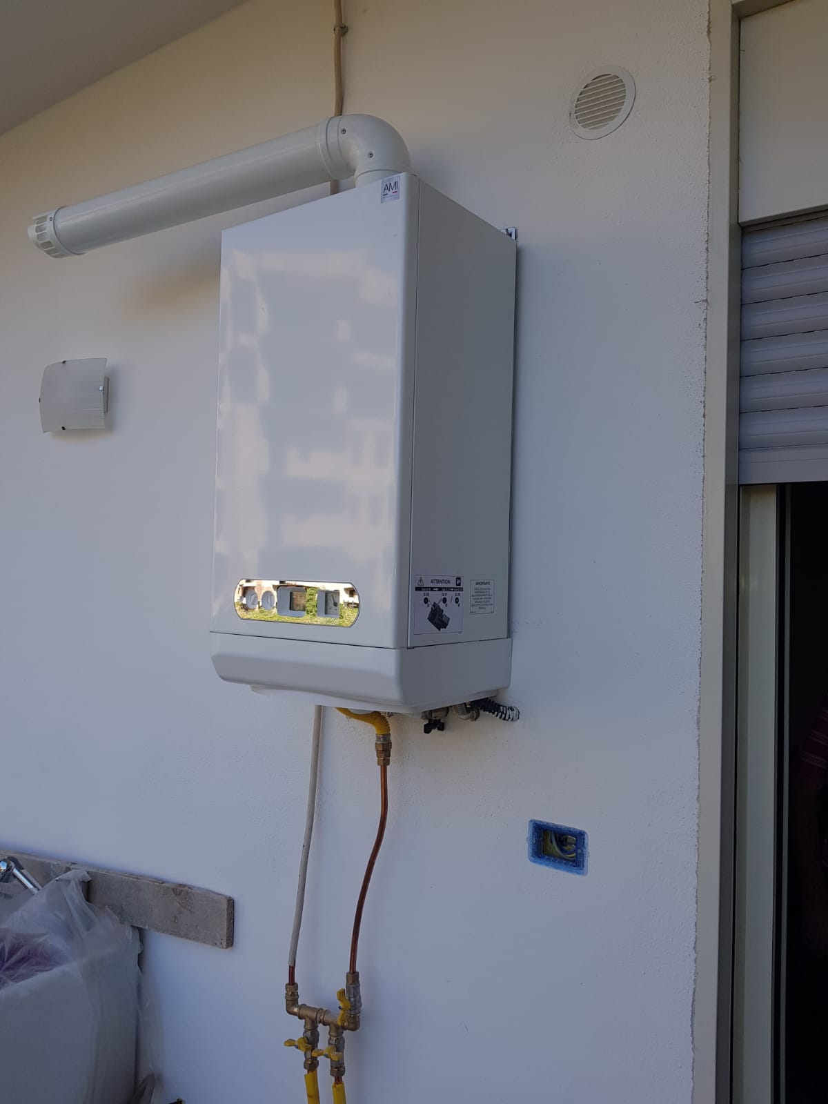 Una caldaia bianca è appesa a una parete bianca accanto a una finestra.