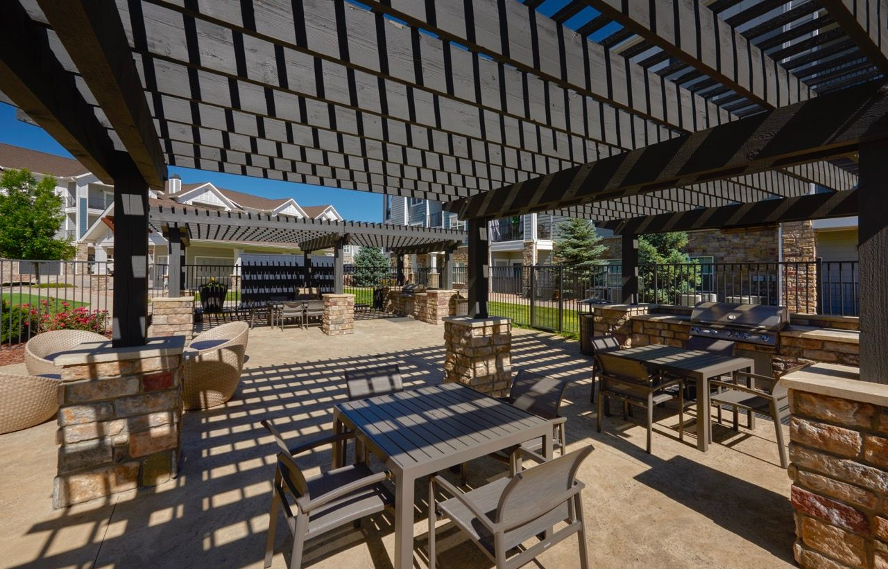 Outdoor communal patio with pergola canopies, seating, and grills at an apartment complex.
