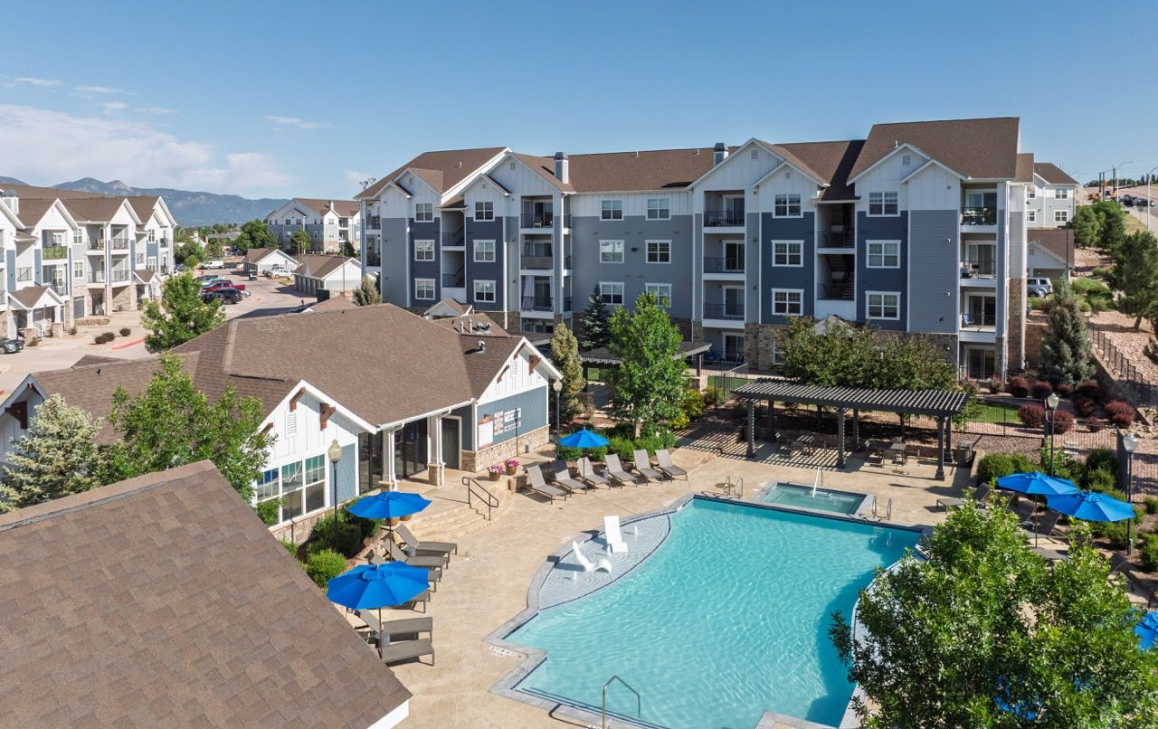 Aerial view of a multi-building apartment complex with a large outdoor pool, lounge chairs, and a shaded cabana area.