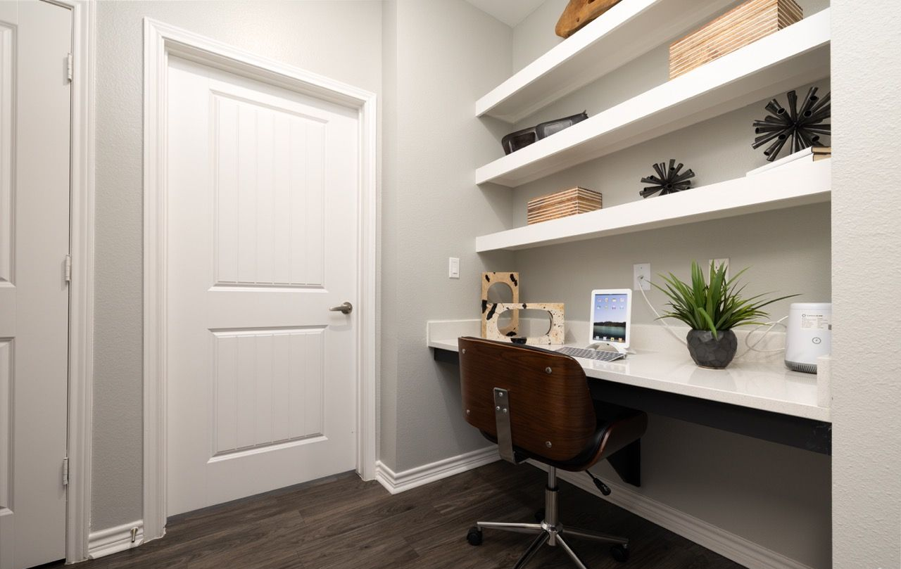 Compact apartment home office with a white desk, chair, and wall shelves.