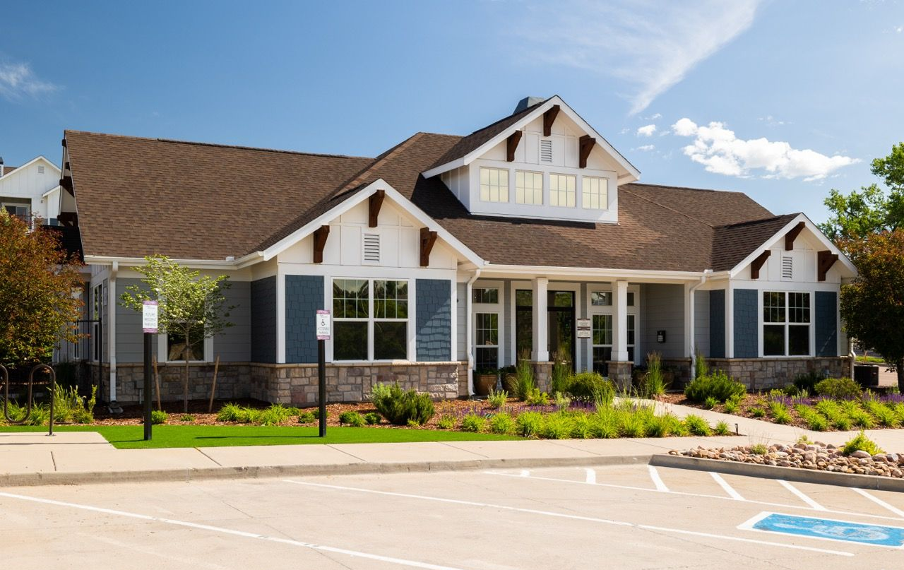 Exterior view of a modern apartment community building with a landscaped front yard and parking lot.