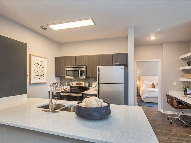 Open-concept kitchen with an island, stainless-steel appliances, and a doorway to a bedroom.