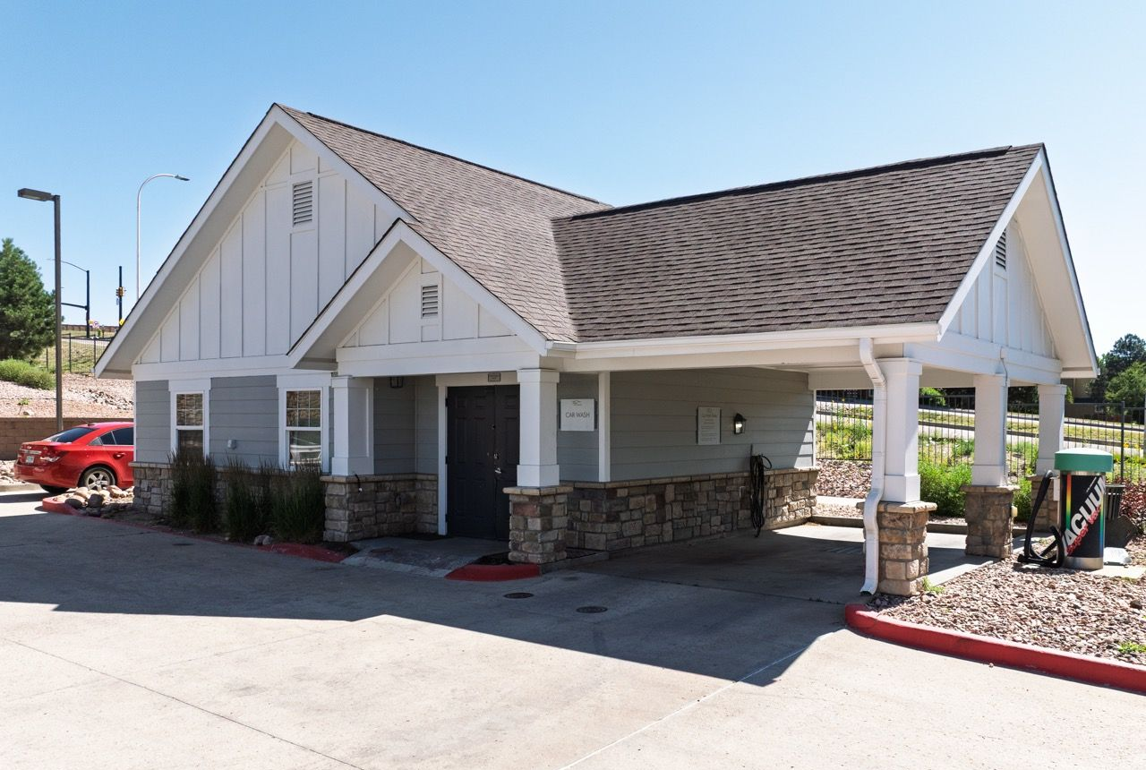 Exterior view of a small community building with a car wash station under a gabled roof.