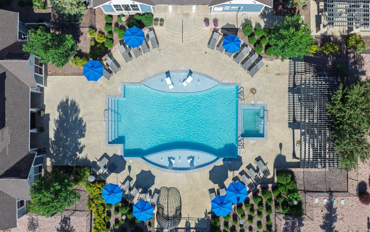 Aerial view of a resort-style apartment pool with blue umbrellas and lounge chairs.