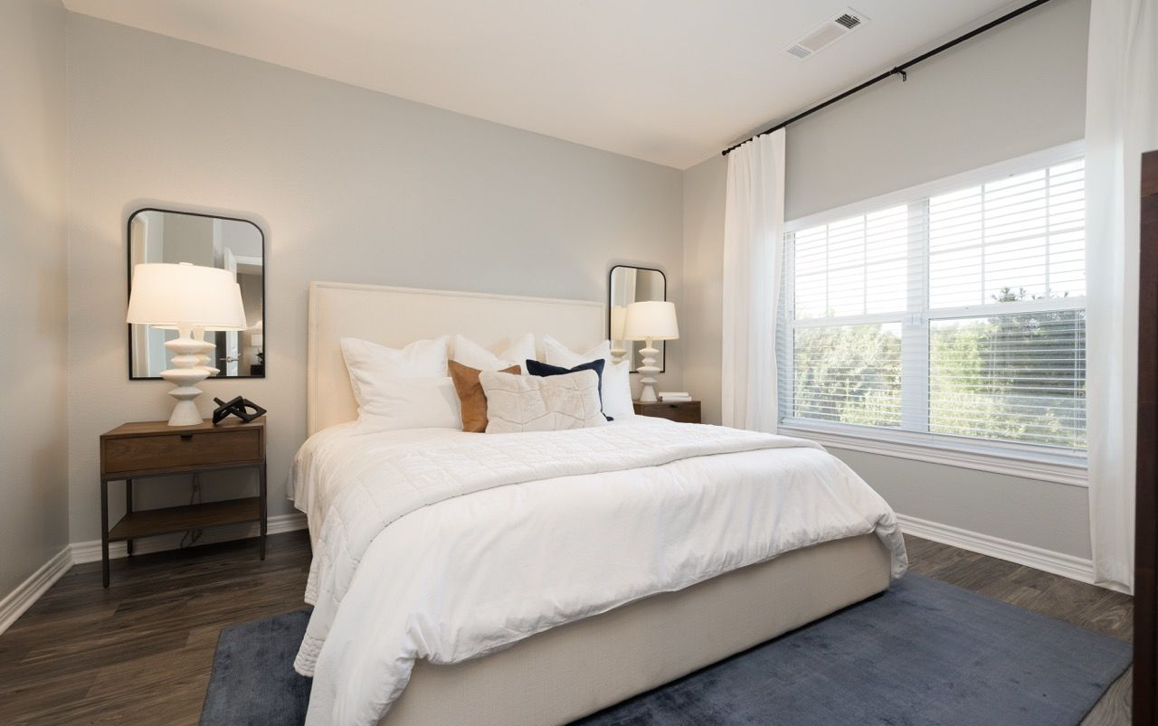 Bedroom in an apartment with a large bed, two nightstands, lamps, and a window.