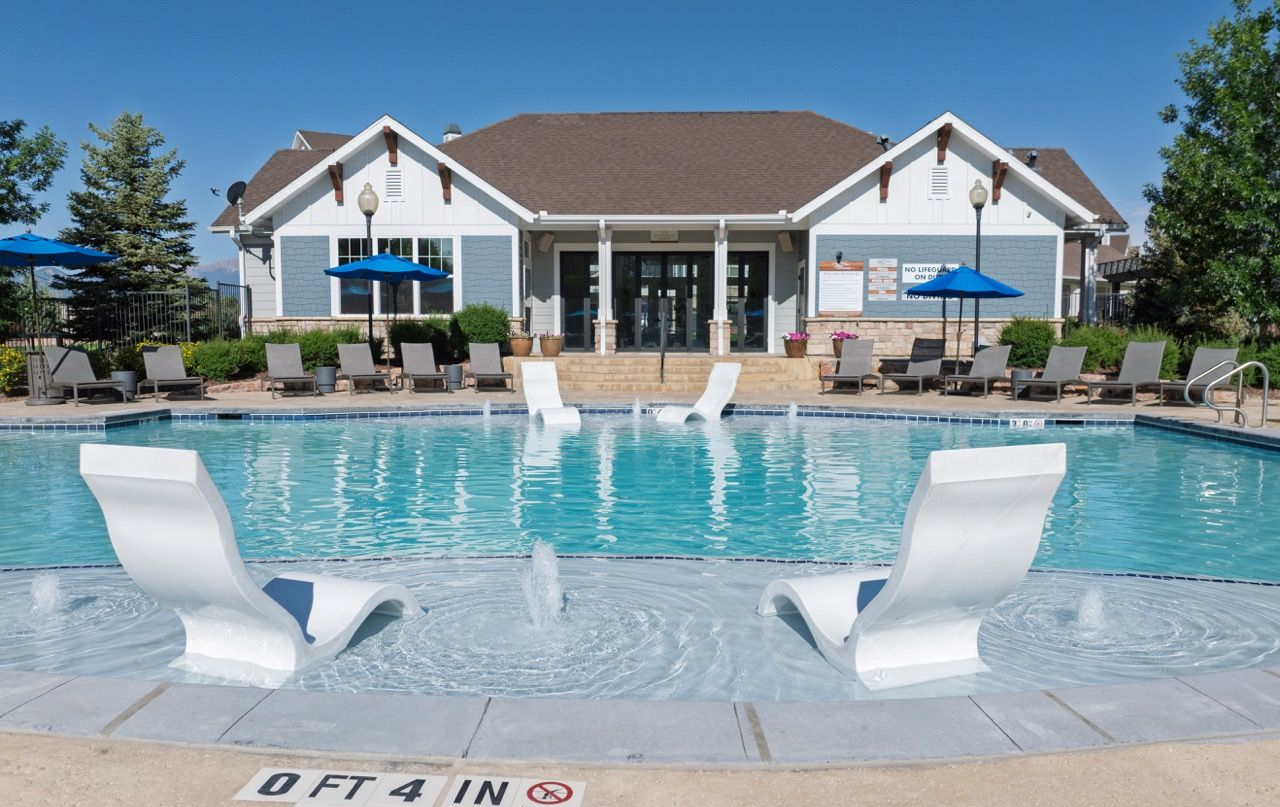 Outdoor apartment community pool with lounge chairs and a clubhouse in the background.